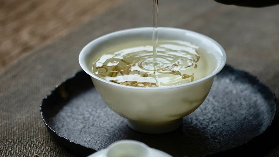 Pouring tea into a white gaiwan, tea leaves floating