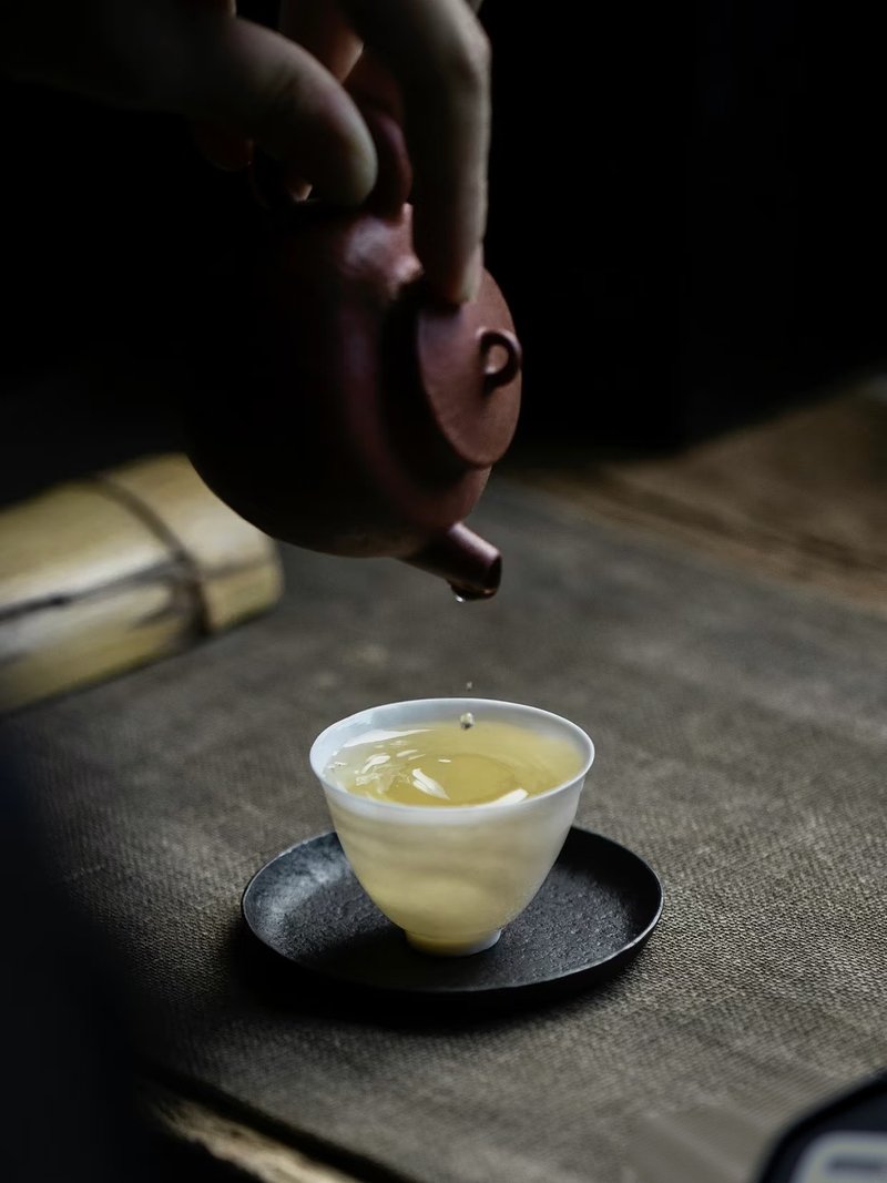 Pouring tea into a small cup from a purple clay teapot